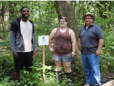 两名学生和一名教师站在自然中心小径附近的标志牌旁